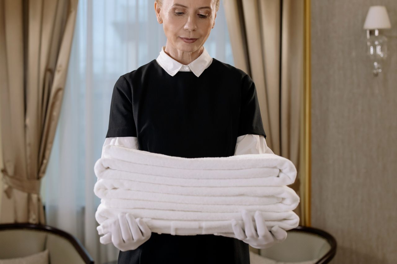 services-05 Professional housekeeper carrying a pile of fresh towels in an upscale hotel room, highlighting elegance and attentive service.